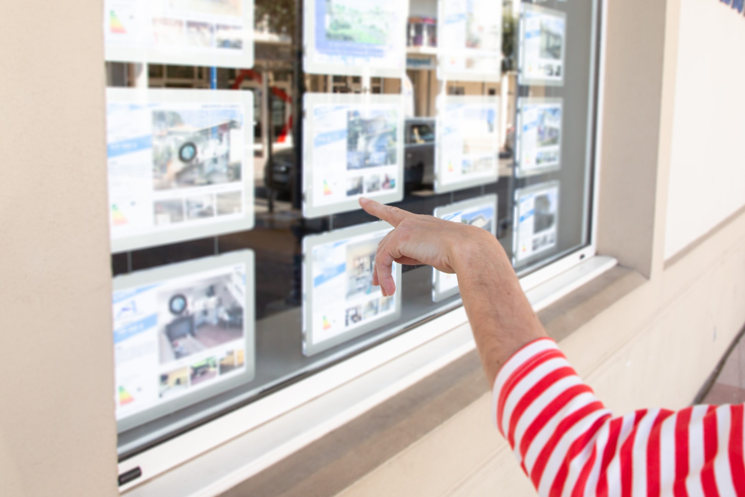 Une femme qui pointe une annonce dans la vitrine d'ne agence immobilière